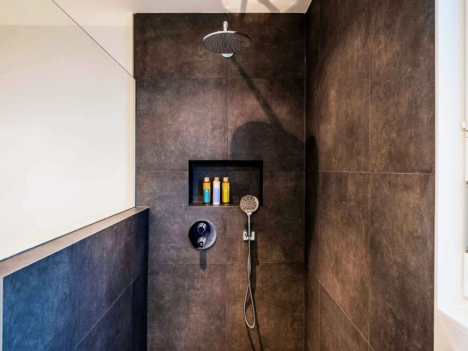 Walk-in shower in large dark wall tiles, with a recessed niche and a rainfall shower head