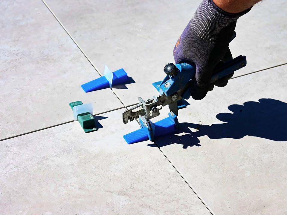 Levelling clips being tightened between large grey floor tiles