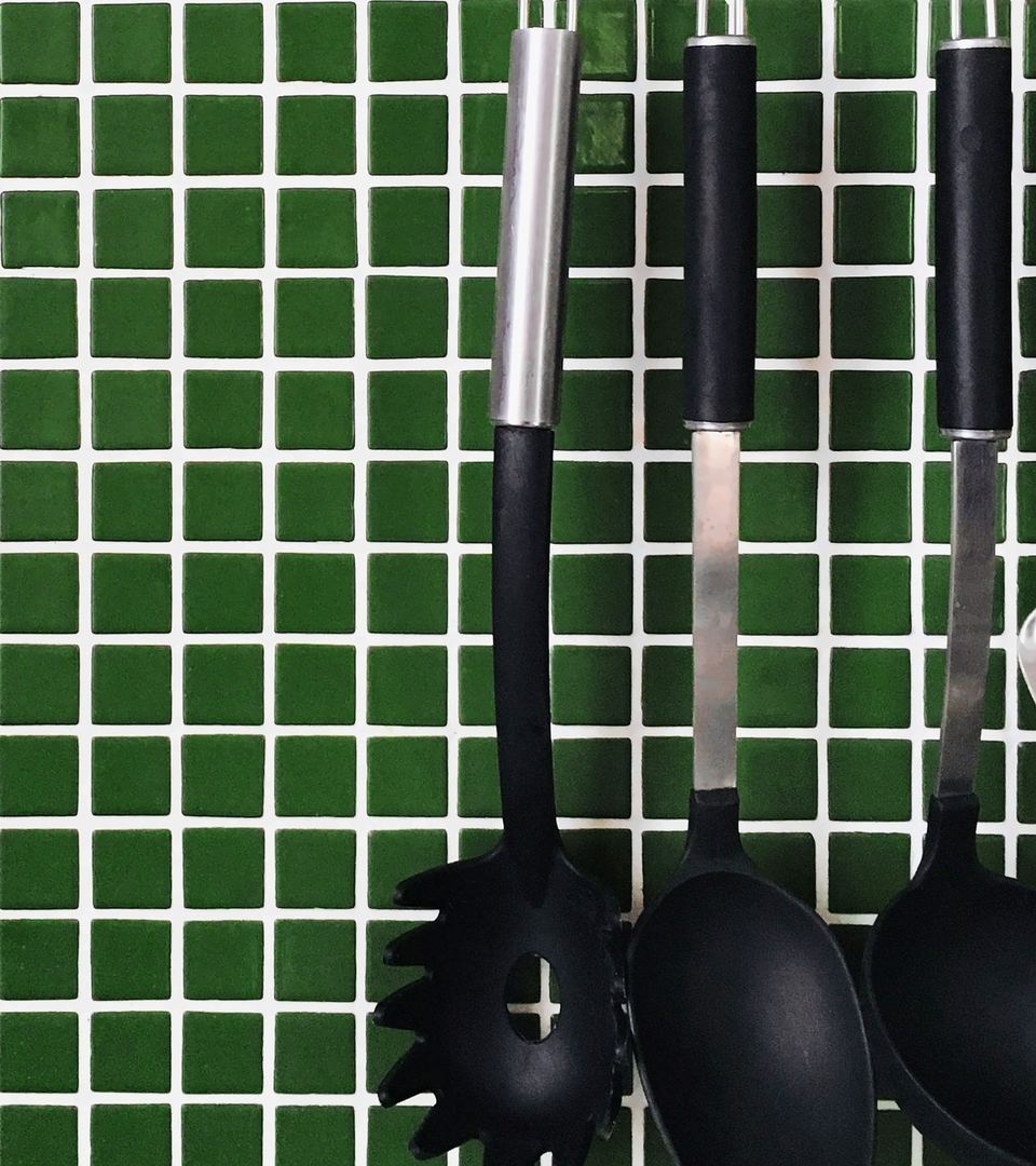 Green square kitchen wall tiles with utensils hanging from a rail