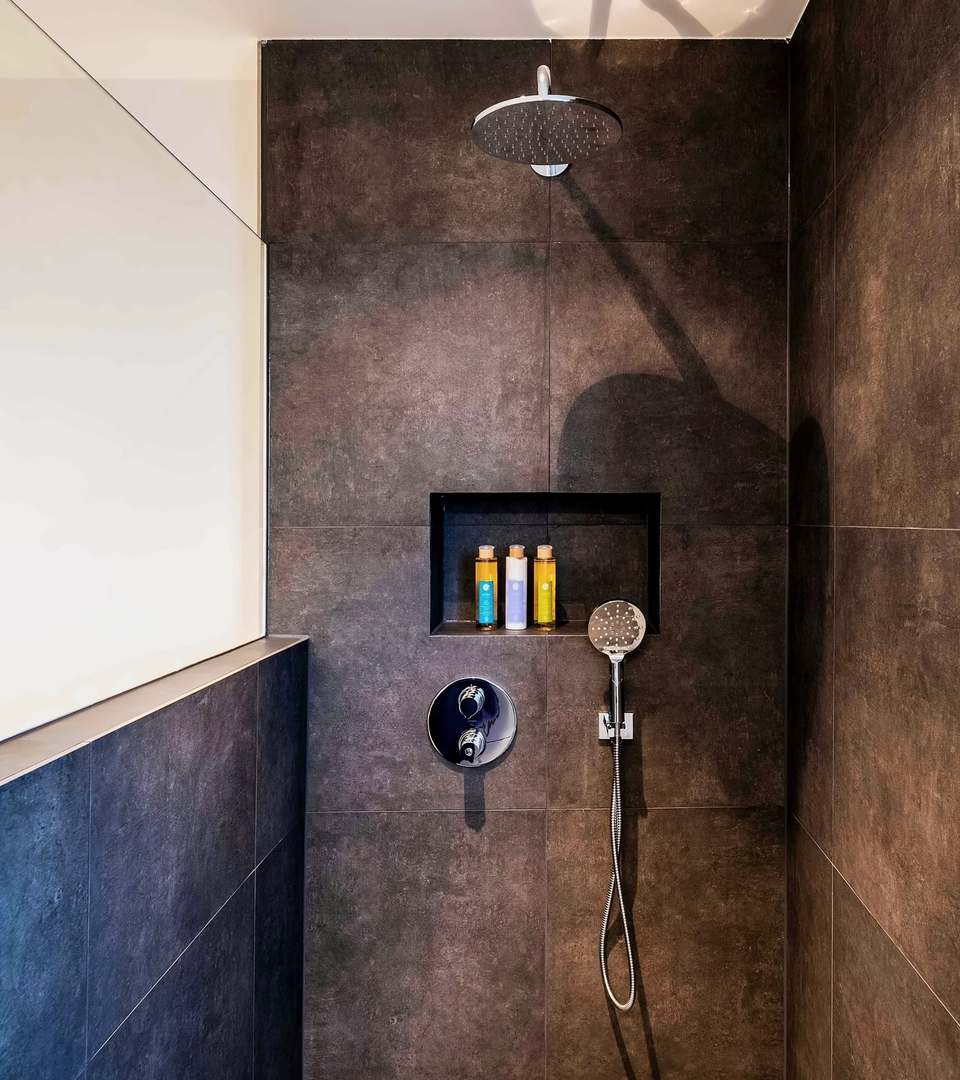 Walk-in shower in large dark wall tiles, with a recessed niche and a rainfall shower head